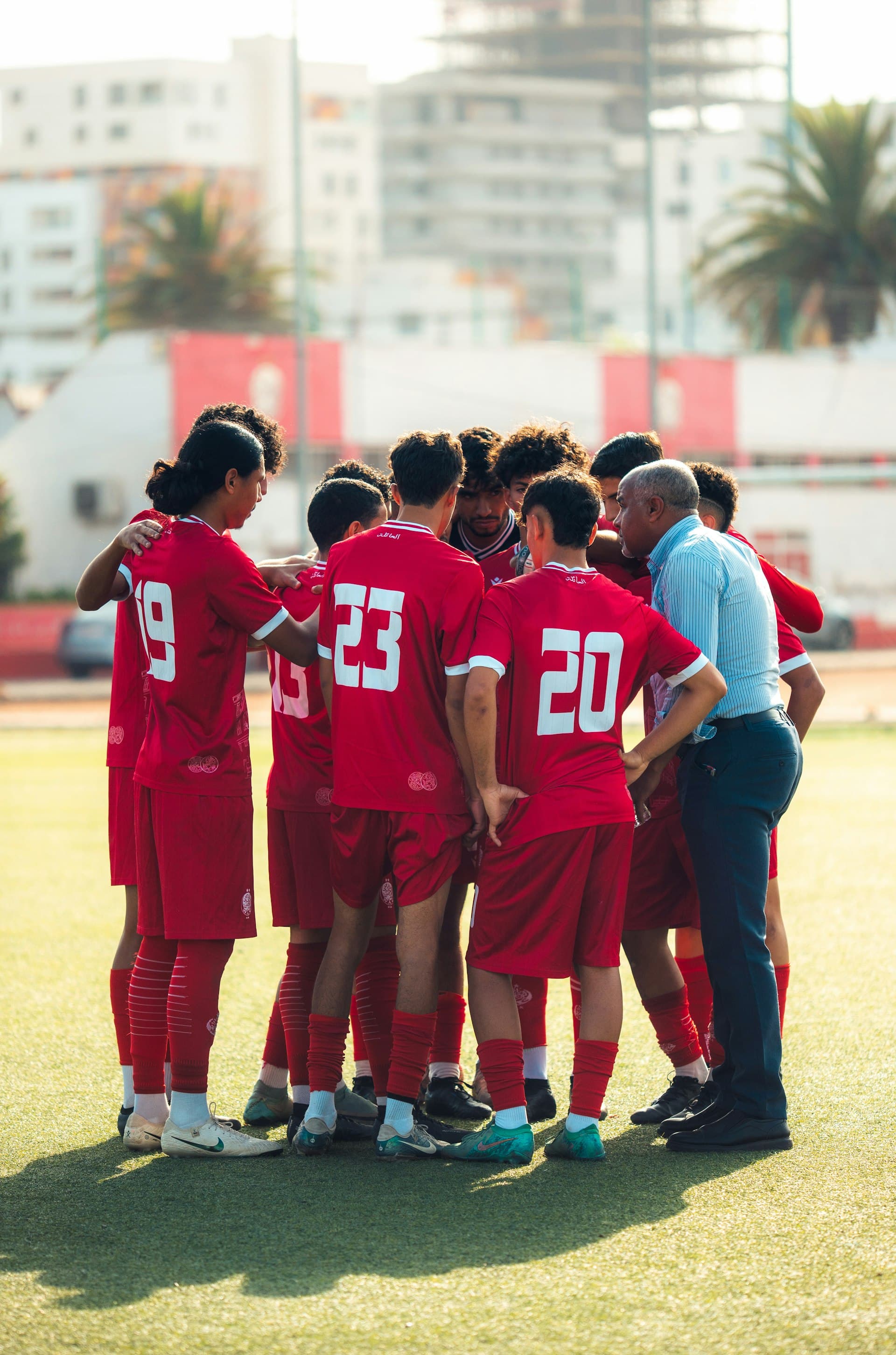 Football coach talking with youth players in a team huddle on the pitch